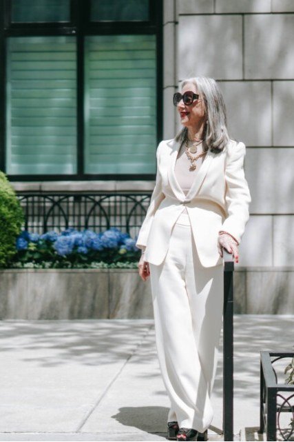 Elegant work outfit for women over 50: cream suit, green shrub background, street