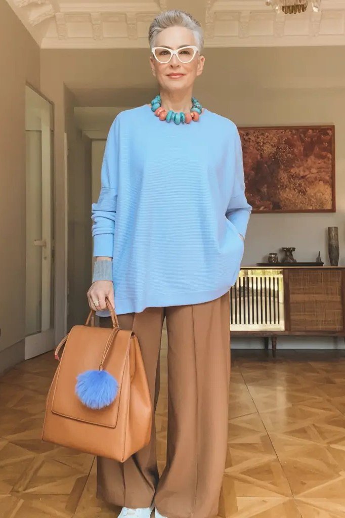 light blue sweater with tan wide trousers, statement necklace and tan bag - fall outfit idea for women over 70