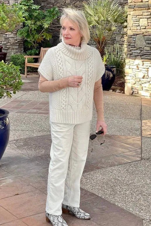 cream cable-knit poncho sweater with white pants, older woman on patio - fall outfit idea for women over 70