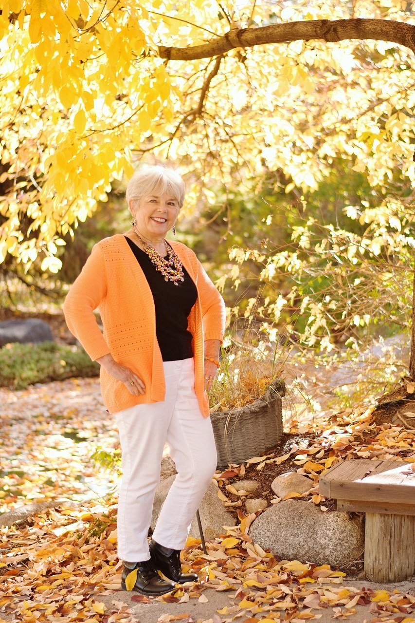 orange cardigan over black top with white pants, fall foliage - fall outfit idea for women over 70