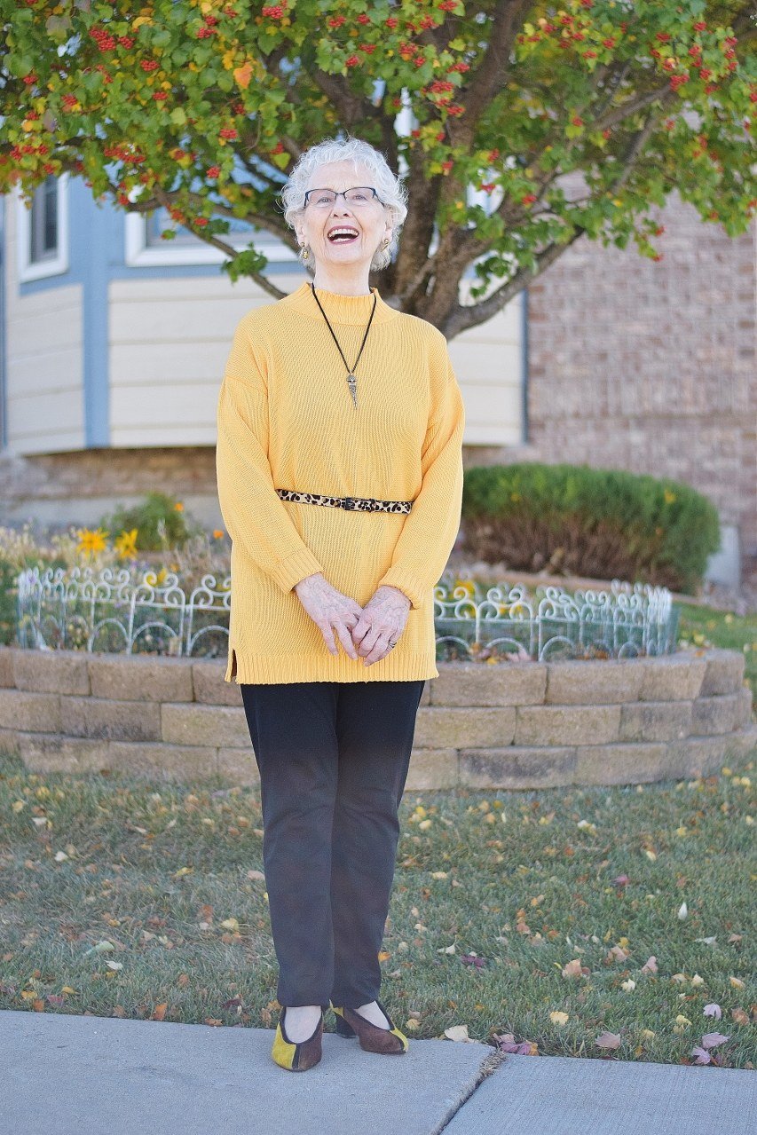 mustard yellow chunky knit sweater with black pants and belt, older woman outdoors - fall outfit idea for women over 70