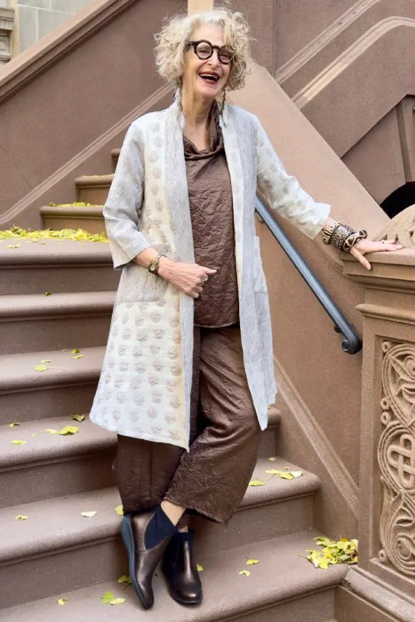 brown patterned long coat over brown top and trousers, woman on stone stairs - fall outfit idea for women over 70