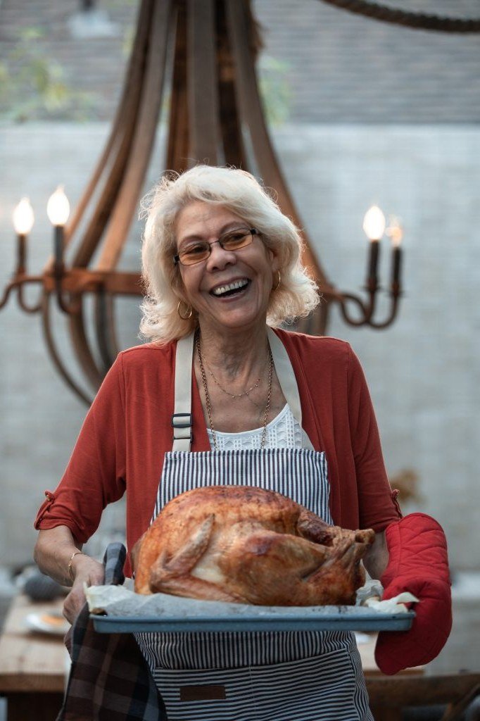 red cardigan with striped apron holding roast turkey, Thanksgiving - fall outfit idea for women over 70