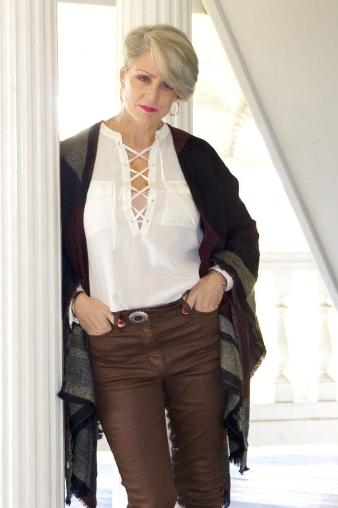 white lace-up blouse with brown pants and dark shawl in doorway - fall outfit idea for women over 70