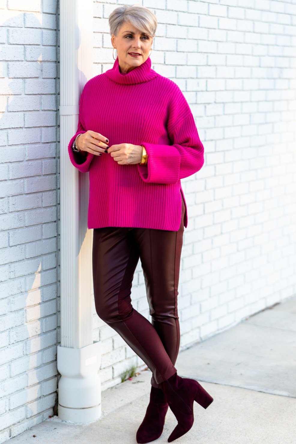 fuchsia turtleneck with brown leather pants and burgundy boots at white brick wall - fall outfit idea for women over 70