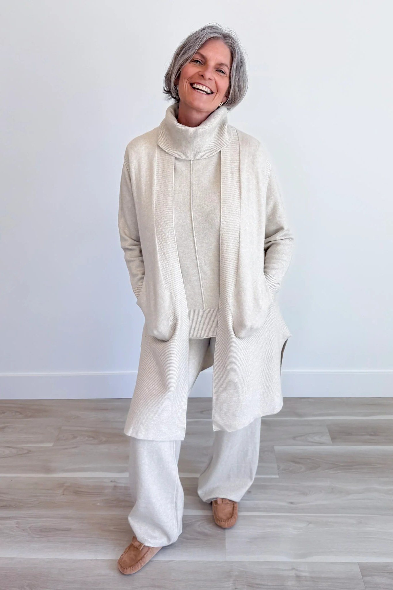 Cream long duster cardigan over cream top and white wide-leg pants, full body front view - fall cardigan outfit idea for women over 60