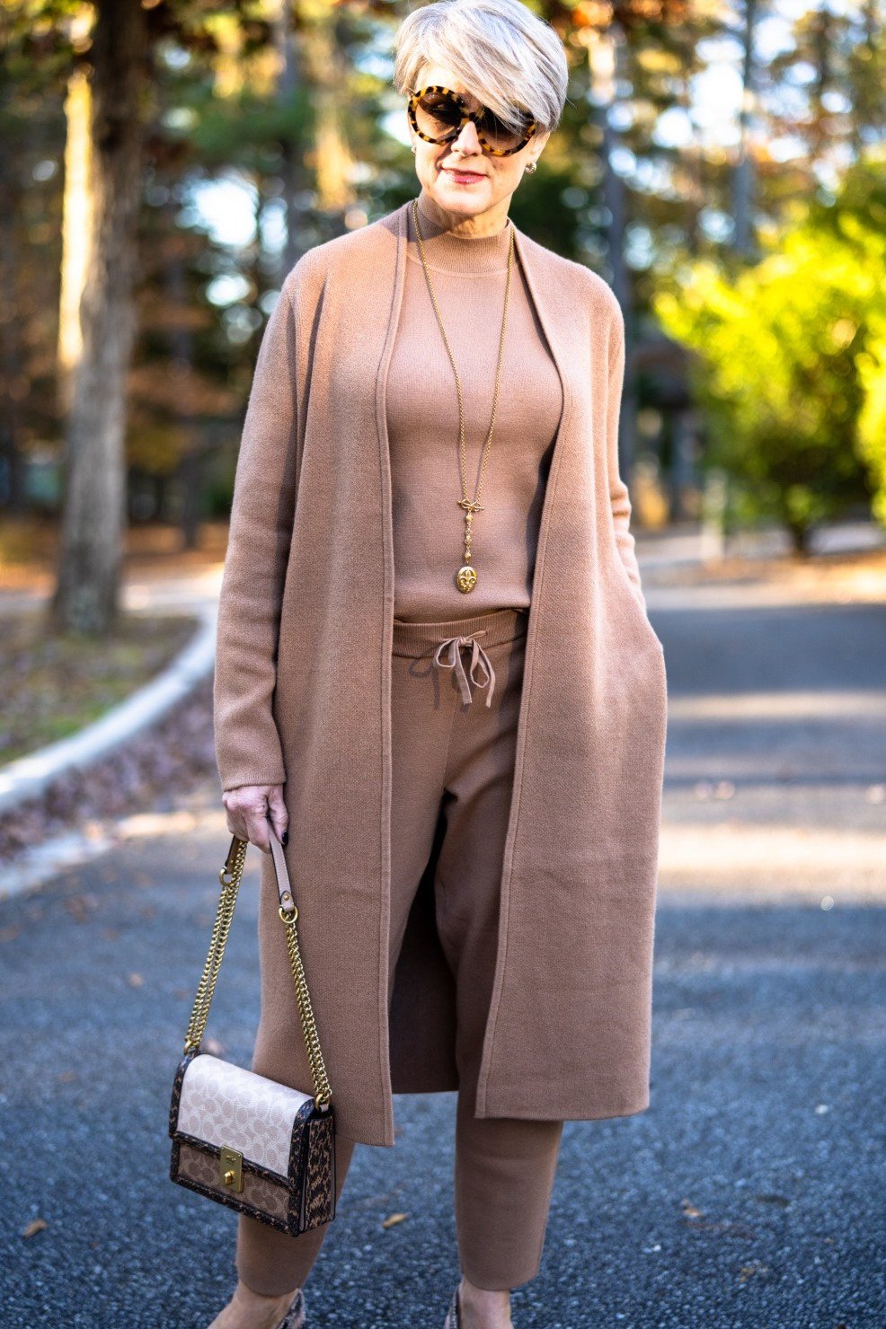 Camel long duster cardigan over camel turtleneck and drawstring joggers, sunglasses and gold necklace, full body front view - fall cardigan outfit idea for women over 60
