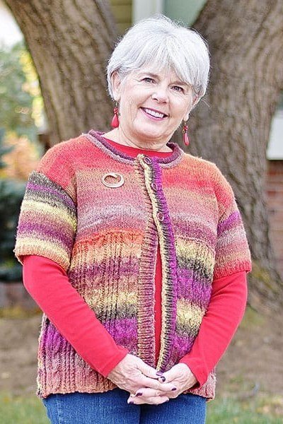 Colorful variegated knit cardigan over red top, jeans, 3/4 front view - fall cardigan outfit idea for women over 60