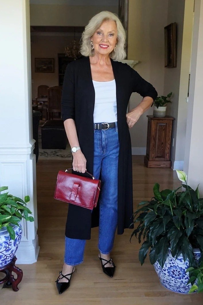 Long black duster cardigan over white top, blue jeans, red bag, full body front view - fall cardigan outfit idea for women over 60