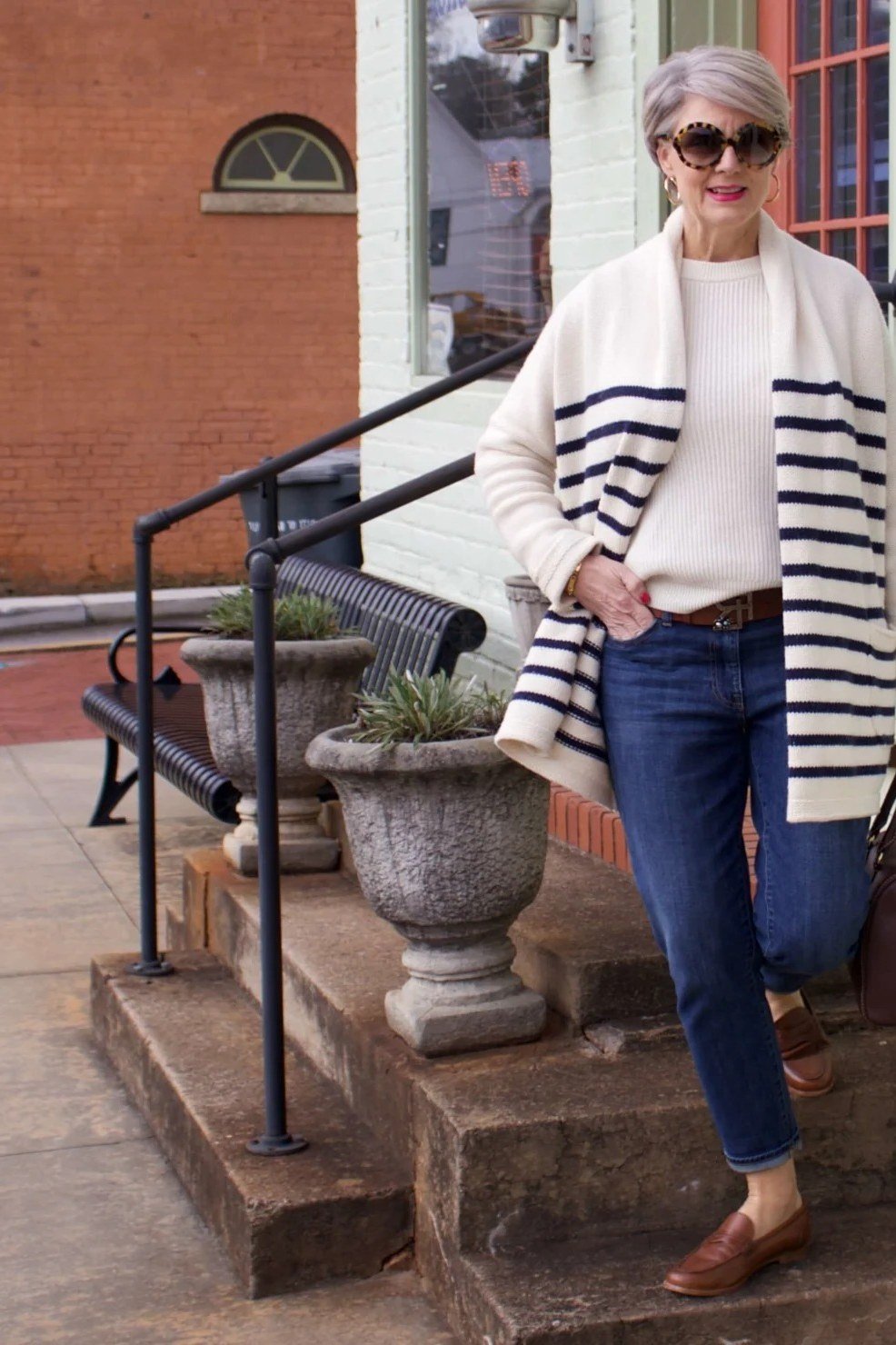 Striped cream/black cardigan over white top, blue jeans, on brick stairs, full body front view - fall cardigan outfit idea for women over 60