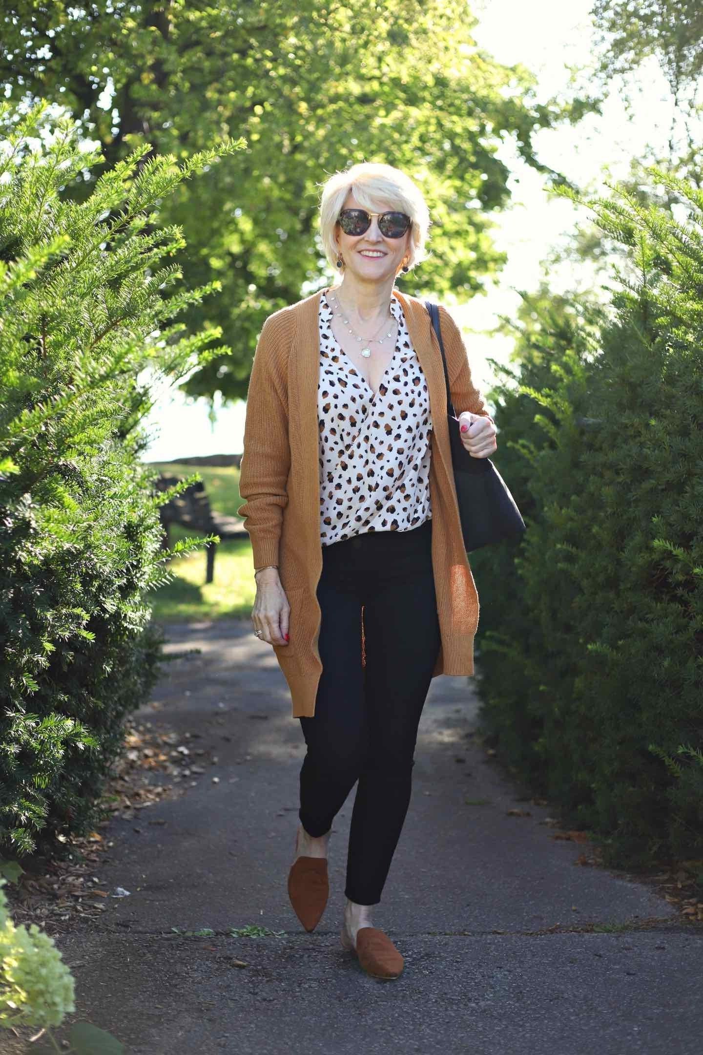 Camel long cardigan over animal-print top, black pants, walking on path, full body front view - fall cardigan outfit idea for women over 60