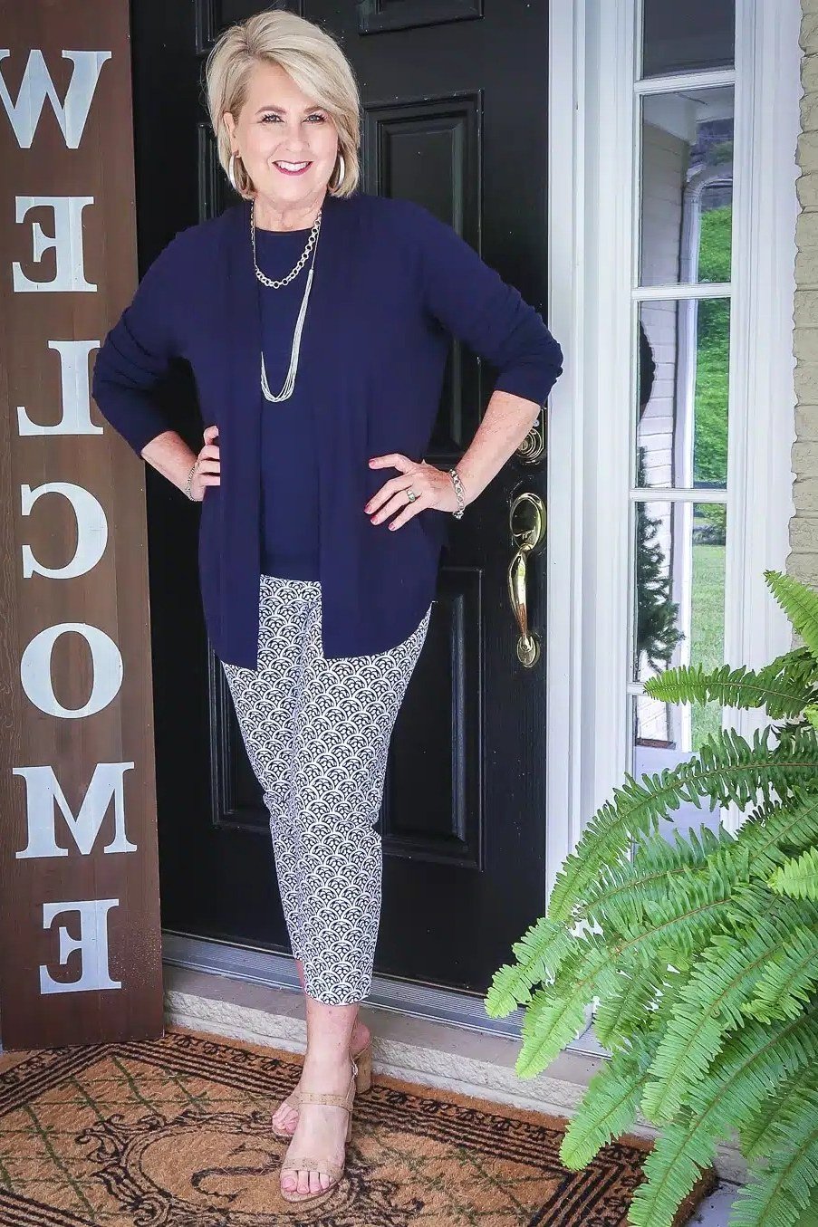 Navy cardigan over navy top, patterned trousers, porch with welcome sign, full body front view - fall cardigan outfit idea for women over 60