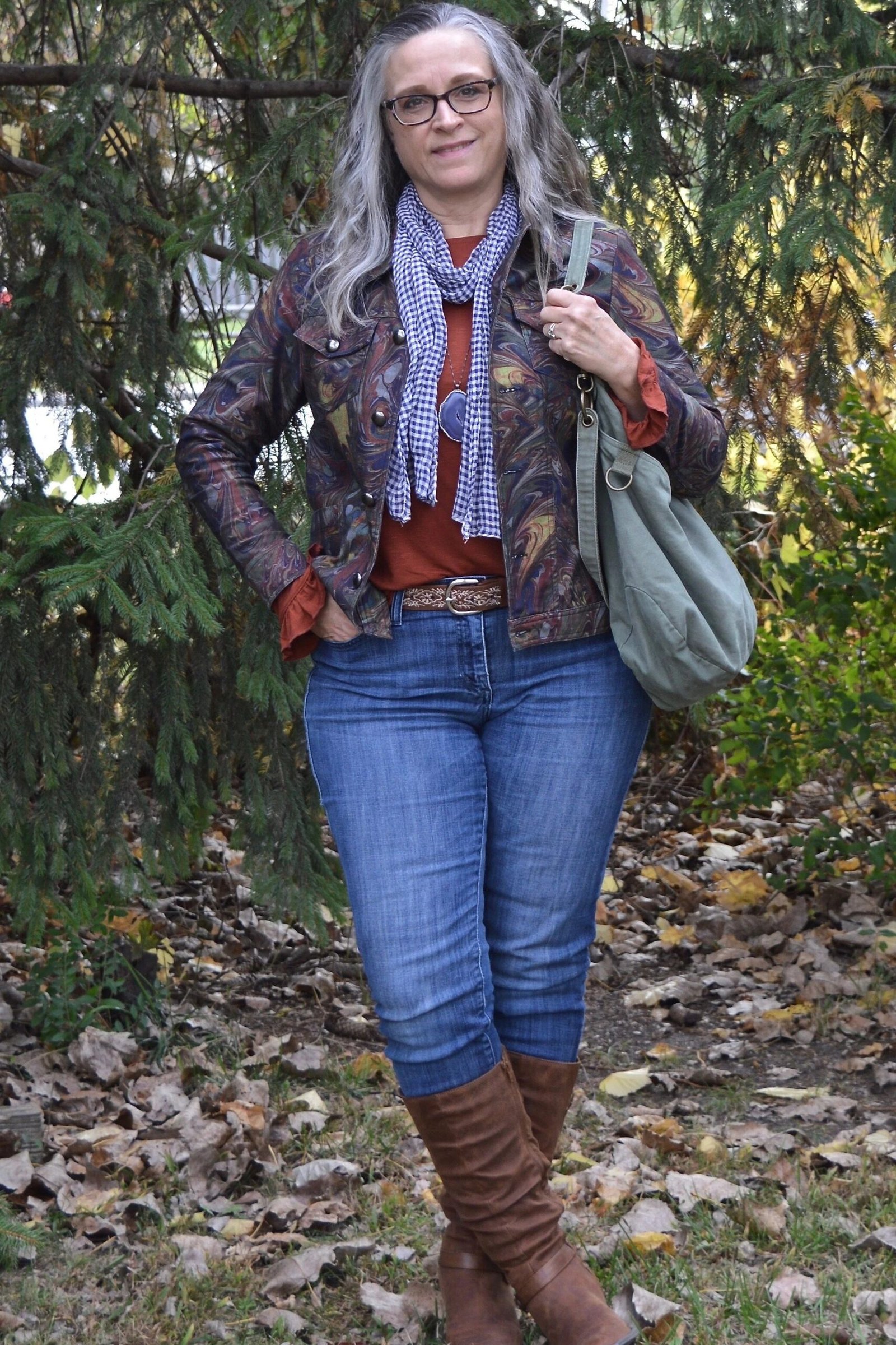Patterned dark cardigan over rust top, blue jeans, brown boots, full body front view, outdoor fall setting - fall cardigan outfit idea for women over 60