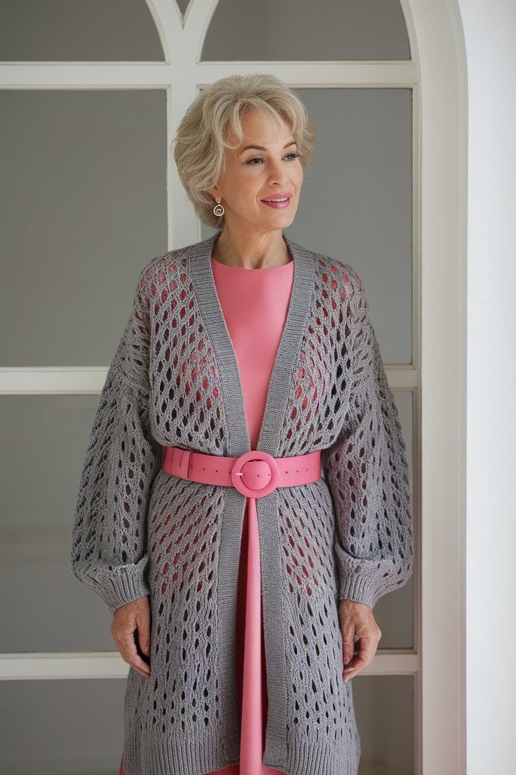 Grey open-knit belted cardigan over pink dress, full body front view, doorway - fall cardigan outfit idea for women over 60