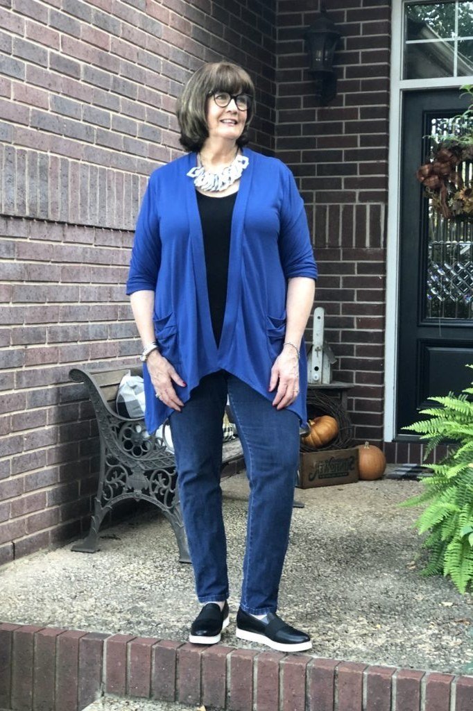 Cobalt blue knit cardigan over black top, blue jeans, sneakers, full body front view, brick porch - fall cardigan outfit idea for women over 60