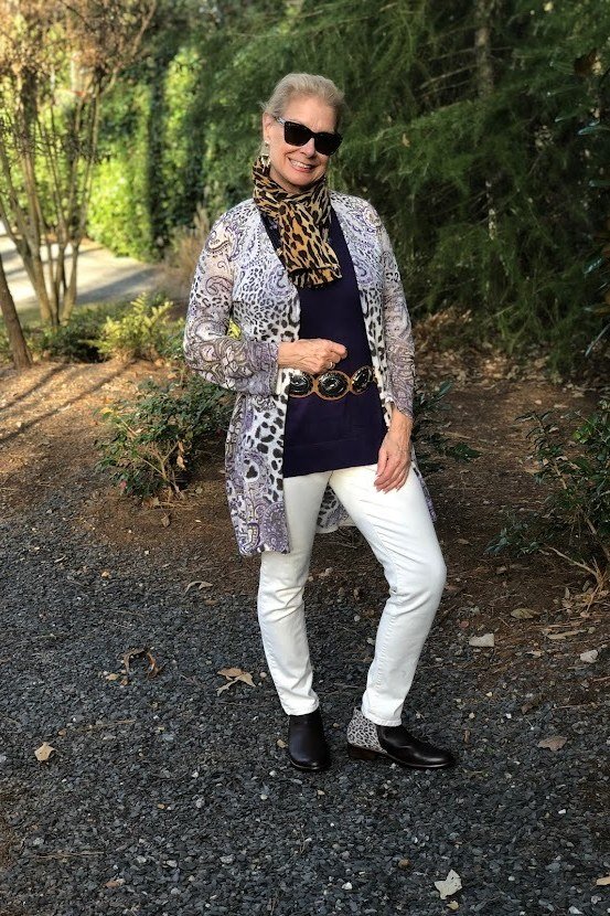 Animal-print knit cardigan over navy top, white jeans, sunglasses, full body front view, gravel path - fall cardigan outfit idea for women over 60