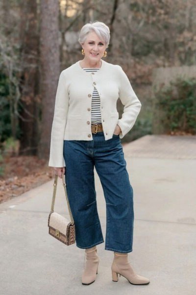 Cream cropped cardigan over striped top, wide-leg blue jeans, beige boots, full body front view, path - fall cardigan outfit idea for women over 60