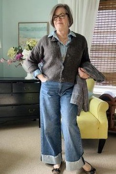 Grey knit cardigan over denim shirt, wide-leg jeans, glasses, full body front view, indoors - fall cardigan outfit idea for women over 60