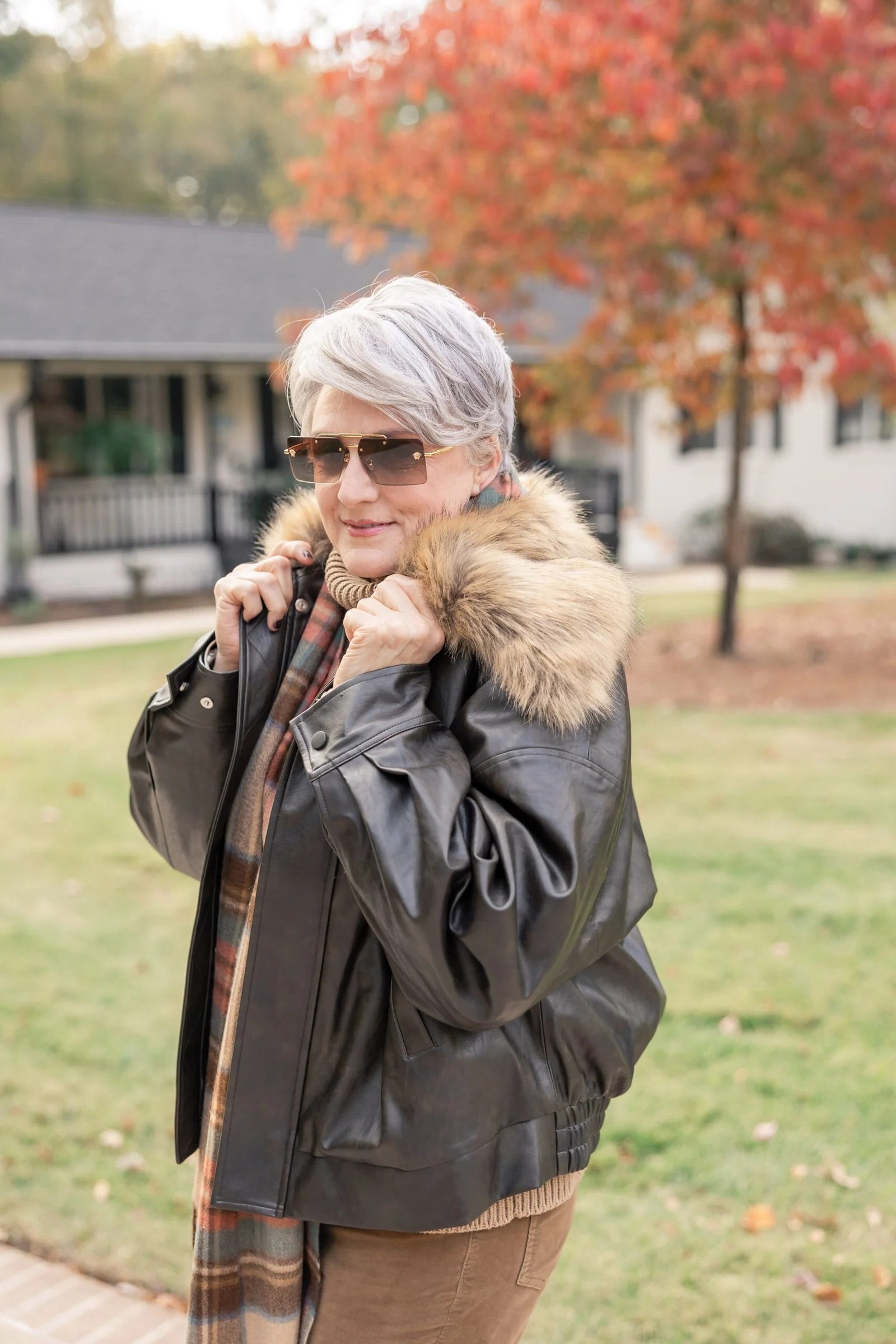 Woman in her 60s wearing a black leather parka coat with a fur-trimmed hood and plaid scarf