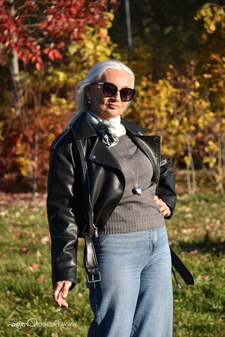Woman in a black moto jacket with a gray sweater and jeans
