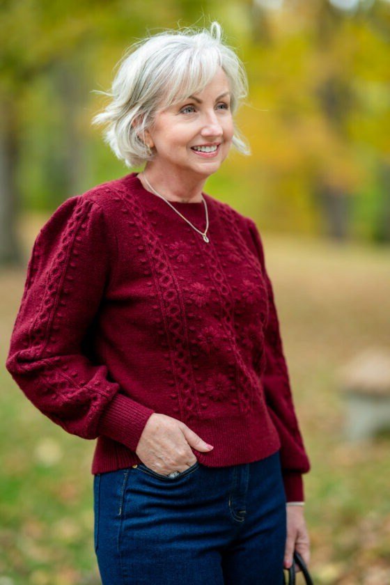 Woman in her 60s wearing a red cable-knit sweater