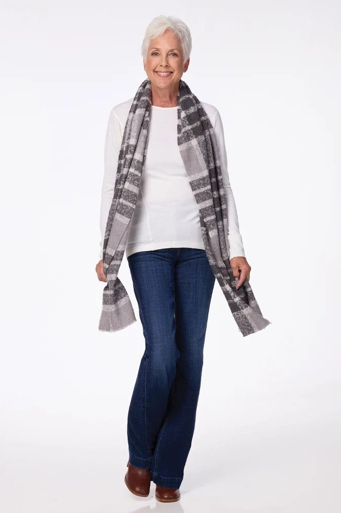 Woman over 60 wearing a white top with a gray scarf and jeans