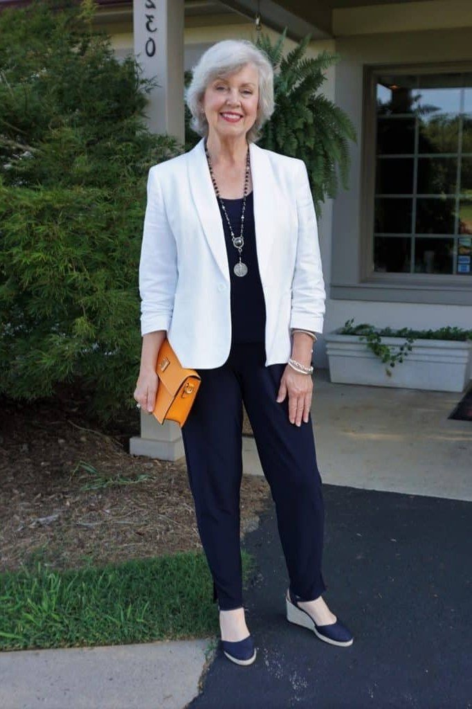 Fall dinner outfit for women over 50: white blazer with navy top and navy trousers, orange clutch