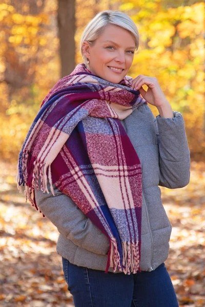Older woman in a gray top with burgundy plaid scarf and jeans in an autumn park - stylish fall look for older women