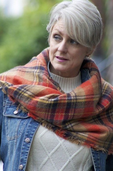 Older woman with a short gray pixie wearing a rust plaid scarf over a denim jacket, close-up - stylish fall look for older women