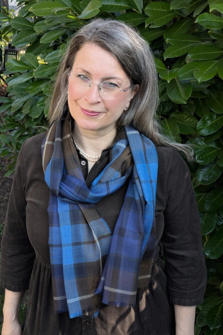 Older woman with a gray bob and glasses wearing a blue plaid scarf and black top - stylish fall look for older women