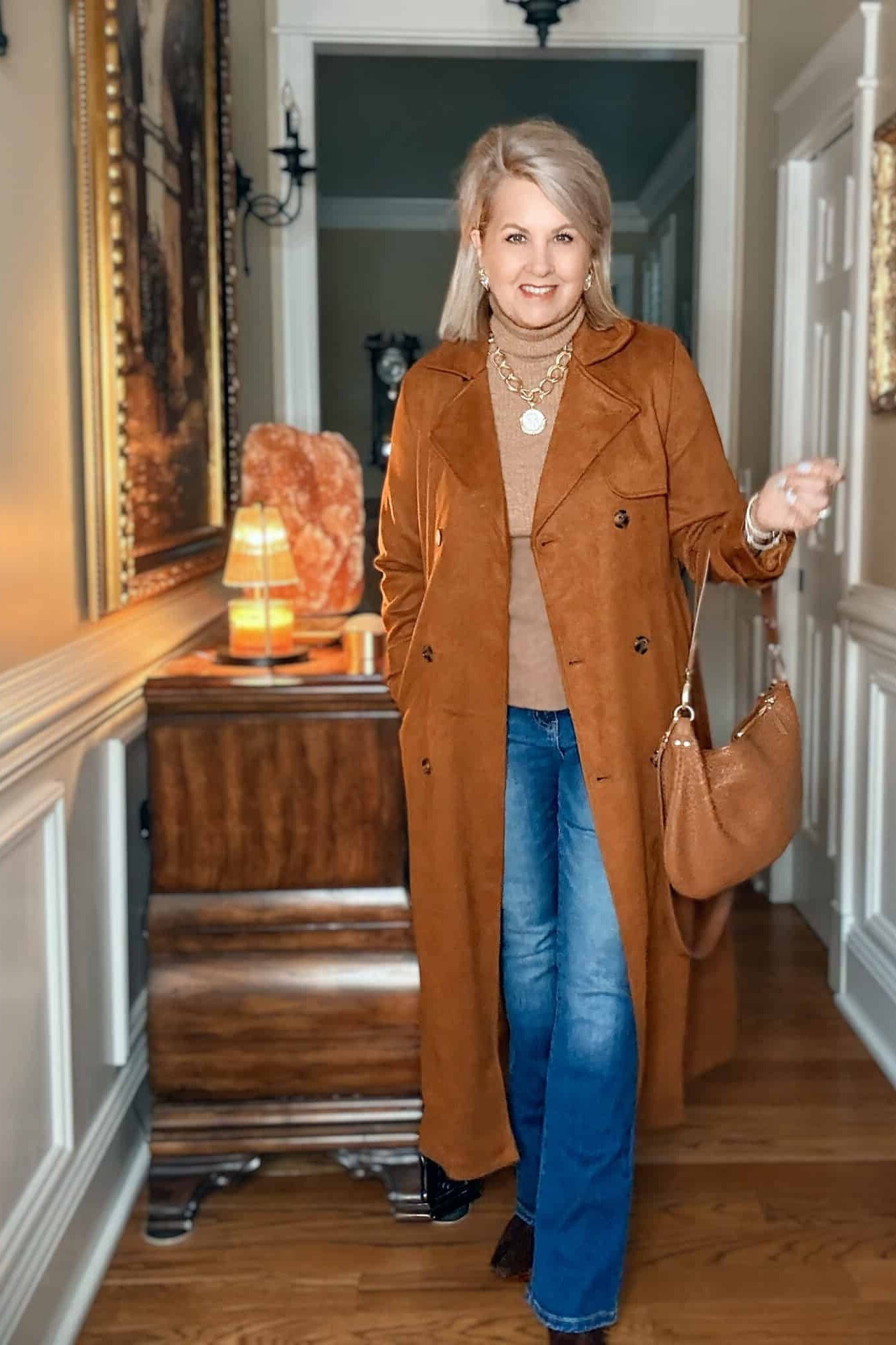 Older woman in a rust-brown coat with jeans in a wooden hallway interior - stylish fall look for older women