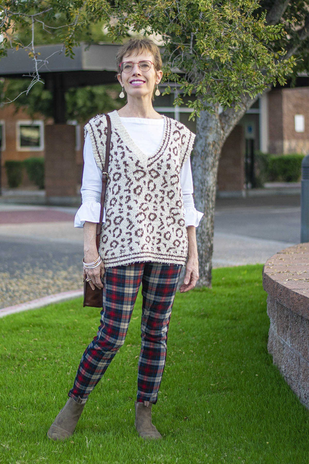 Older woman in a leopard-print vest with a white top and red plaid trousers on a lawn - stylish fall look for older women