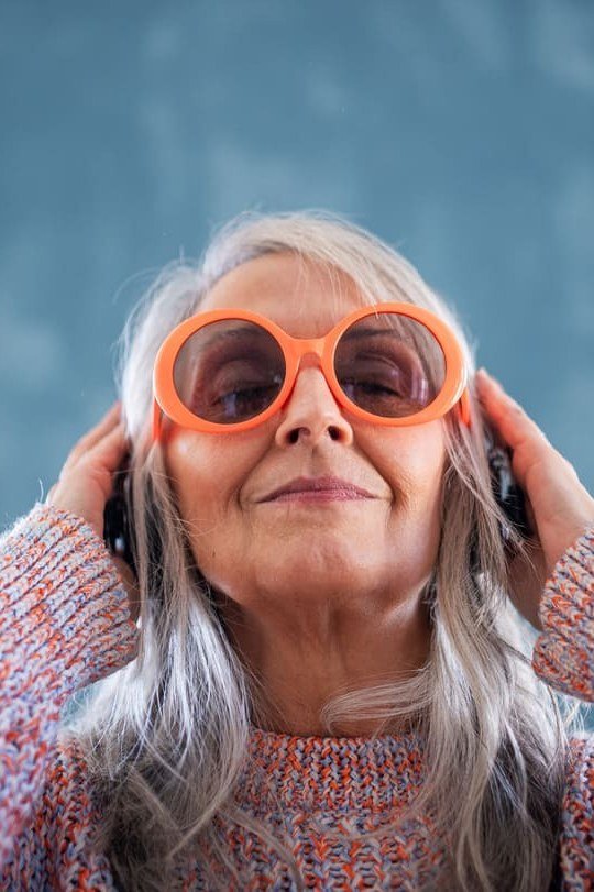 Close-up of an older woman in a pink knit sweater with oversized orange sunglasses - stylish fall look for older women