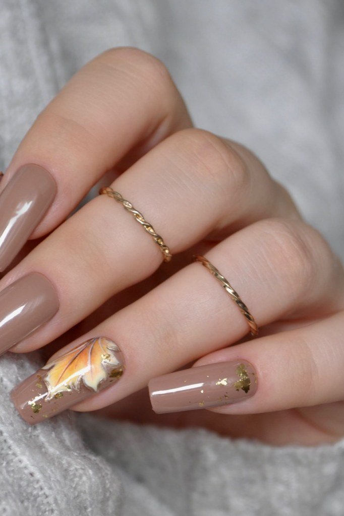 Nude almond nails with a delicate autumn leaf accent