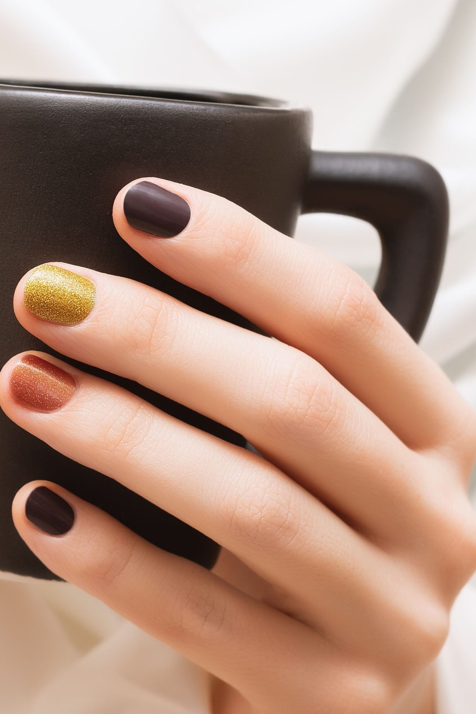 Dark green nails with gold accents holding a coffee mug