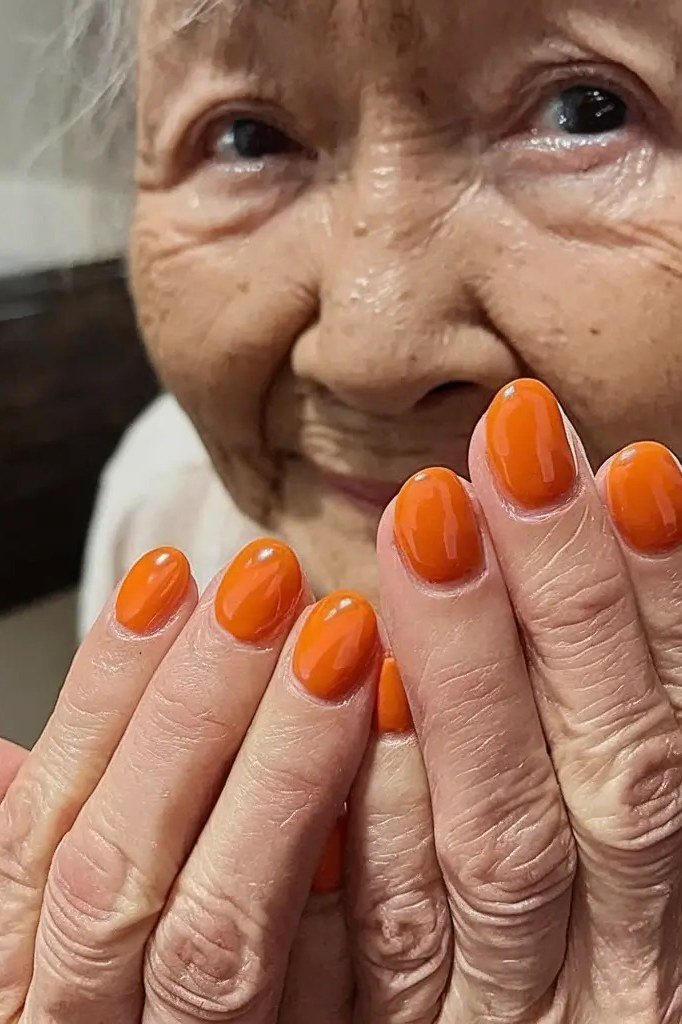 Smiling older woman showing bright orange nails