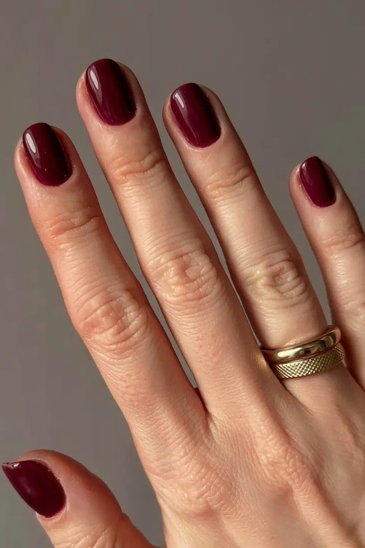 Burgundy short oval nails with gold ring for women over 60