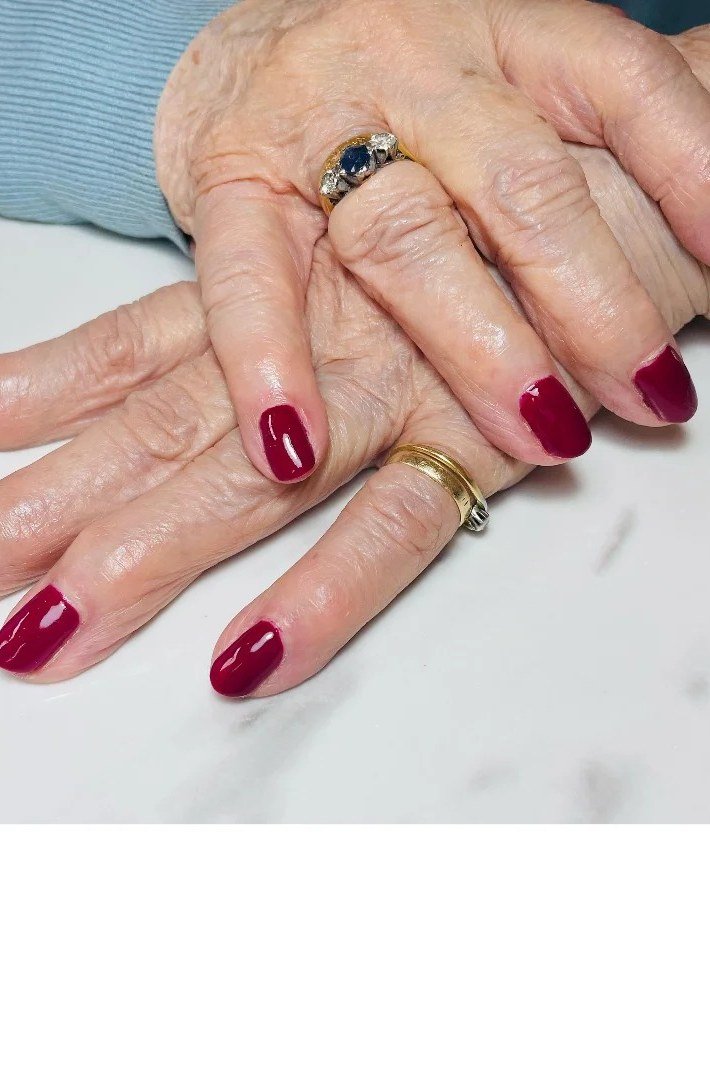 Cranberry nails with gold rings on mature hands for women over 60