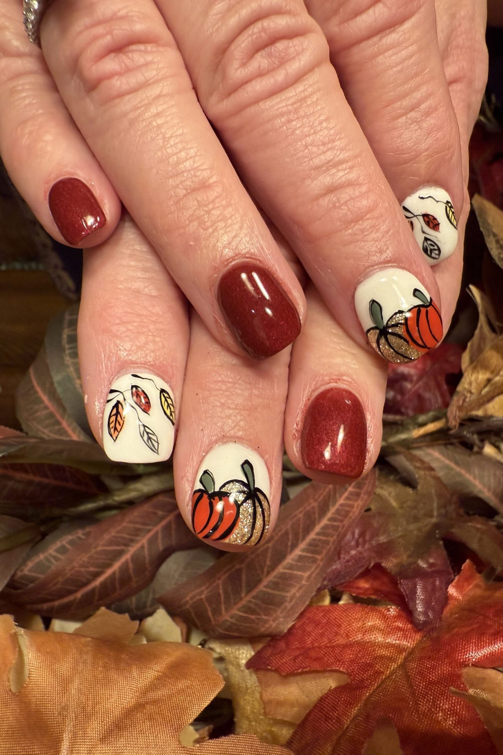 Burgundy nails with pumpkin and leaf nail art accents