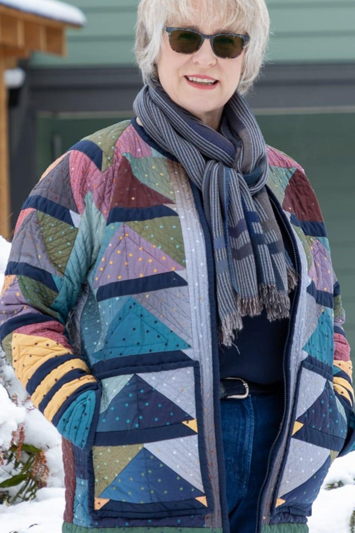 Colorful patchwork quilted jacket with gray scarf and jeans in snow