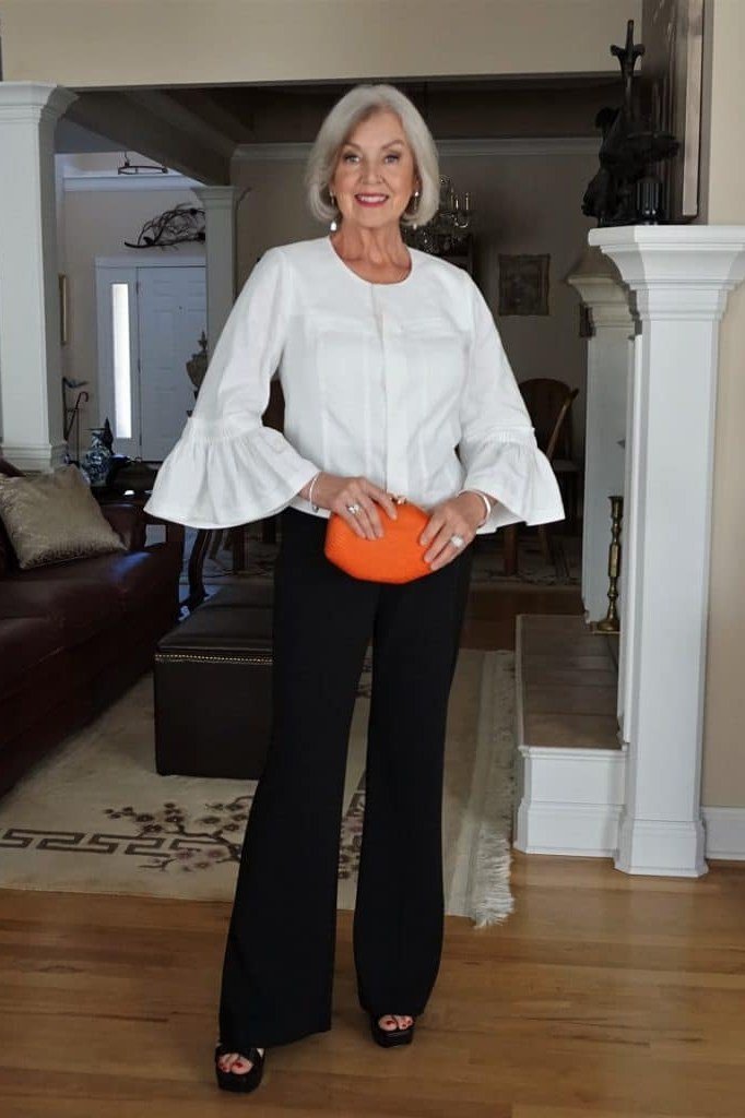 white bell-sleeve blouse with black trousers and orange clutch, fall work outfit for women over 50
