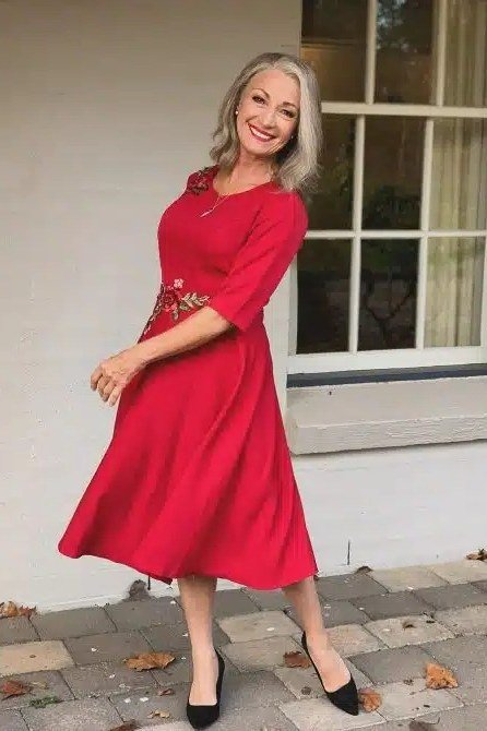 Red twirl fit-and-flare dress for women over 60 on blonde older woman on a porch