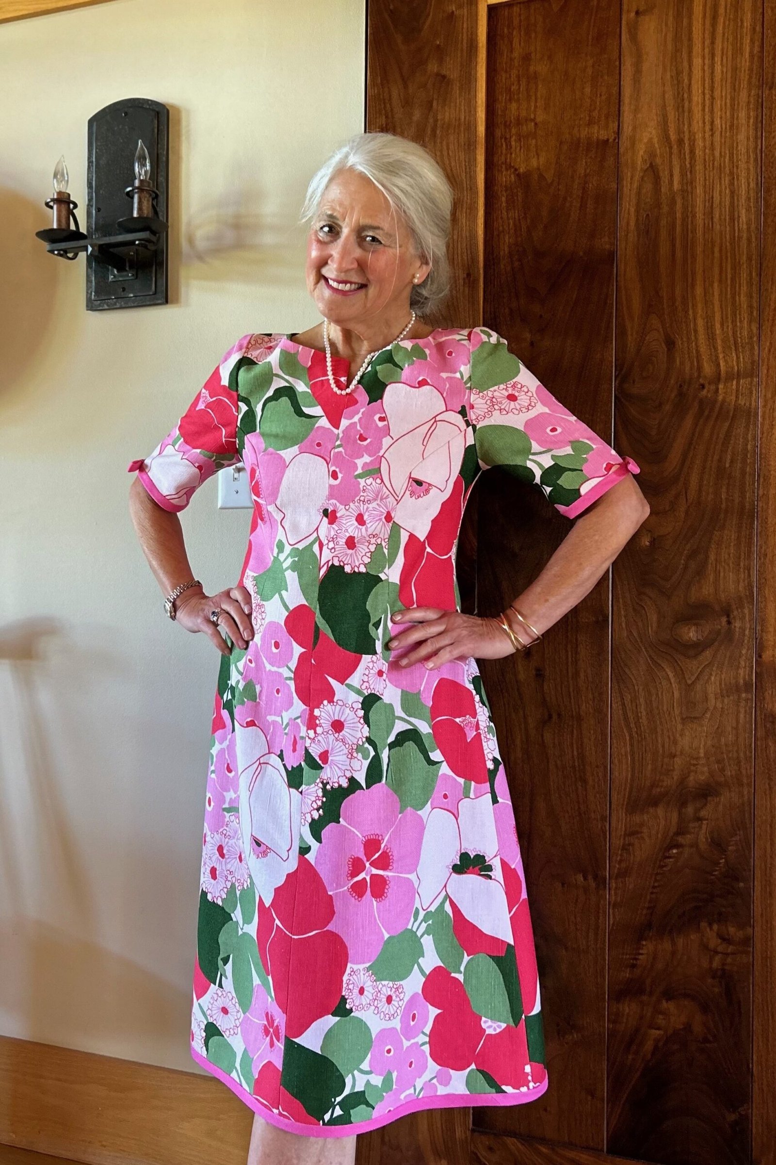 Pink and green bold floral fit-and-flare midi dress for older women by wooden door