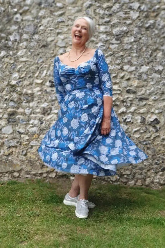 Blue floral twirl fit-and-flare dress for older women outdoors against stone wall