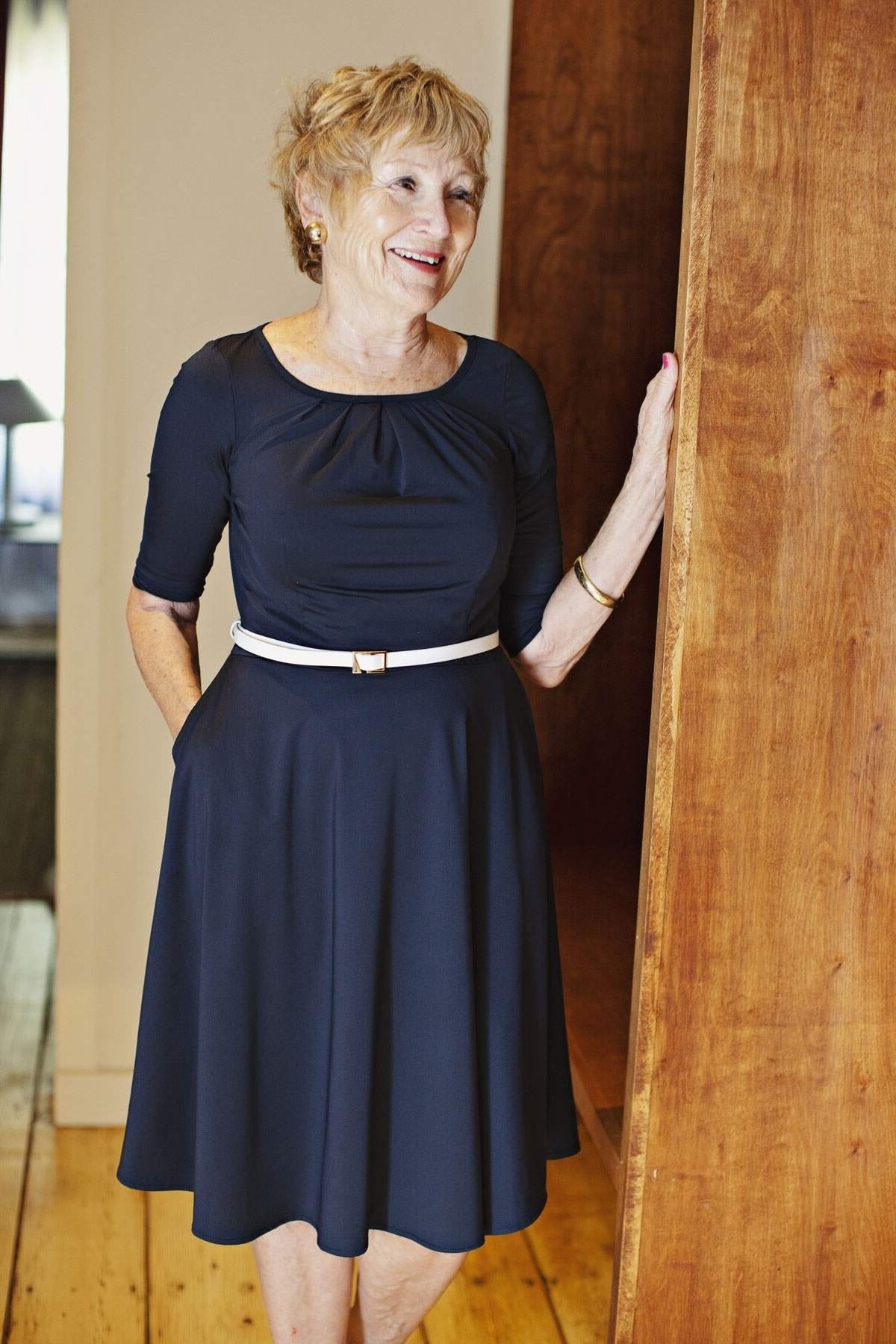Navy fit-and-flare dress with white belt for women over 60 by wooden door