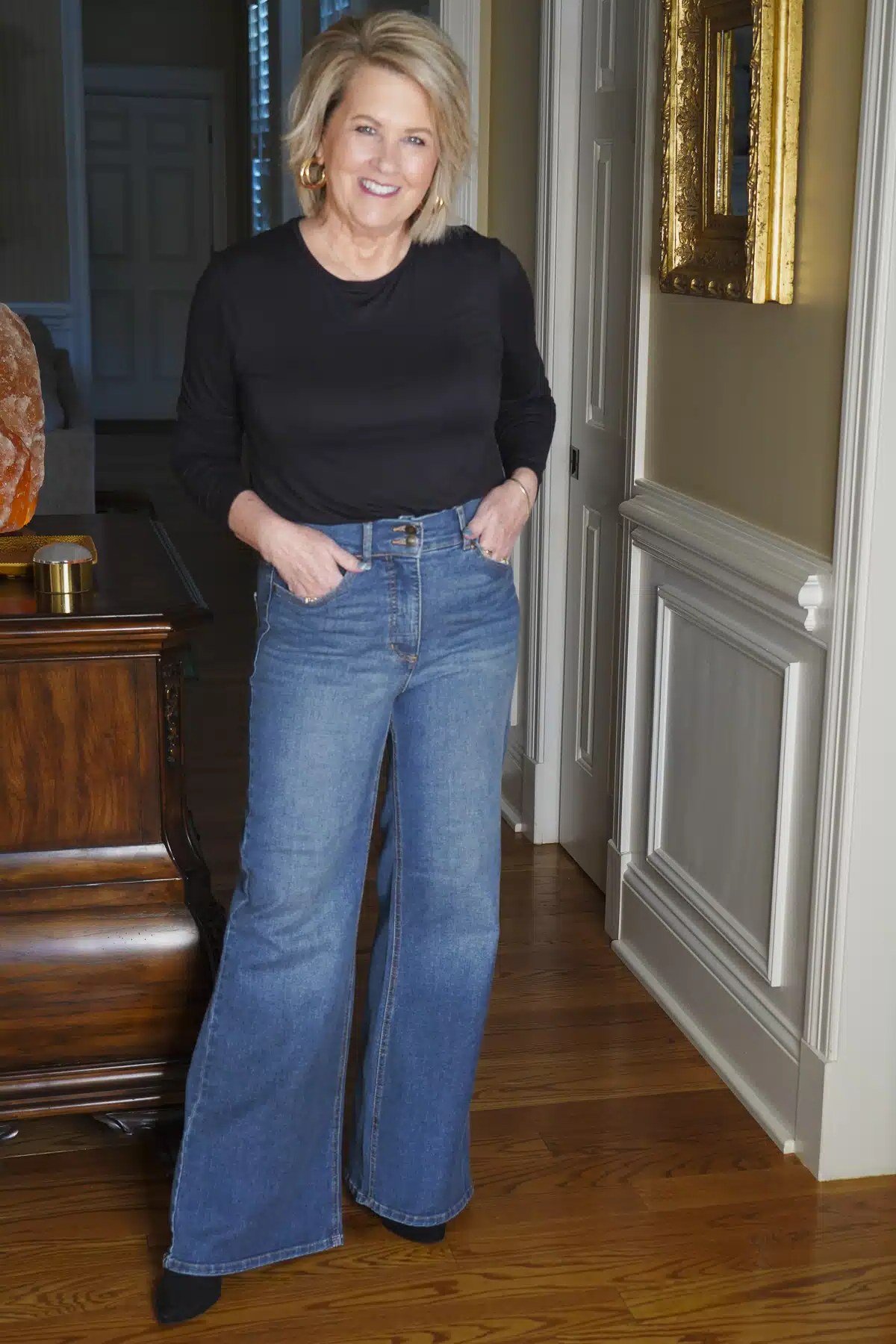 A simple black long-sleeve top tucked into medium-wash wide-leg jeans is easy chic. Hands in pockets, relaxed posture, done. The dark top keeps the eye moving down the long denim line. It works for travel, shopping, or a casual office.