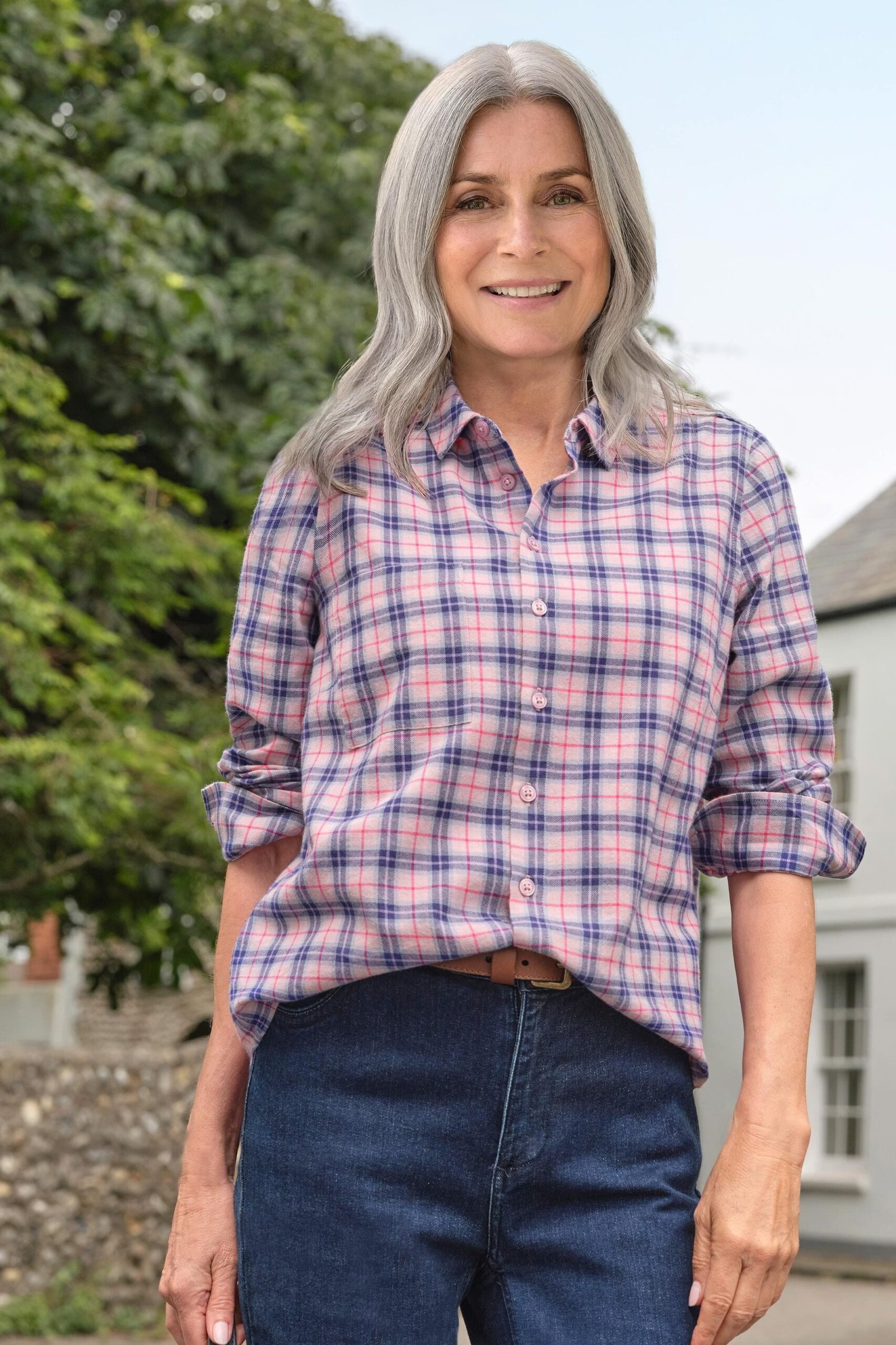 A pink-and-blue plaid shirt with dark jeans is cheerful and easy. Outdoors, the colors pop against fall greenery. The classic button-front fit is relaxed through the body. A no-fuss outfit for errands, walks, or casual Fridays.