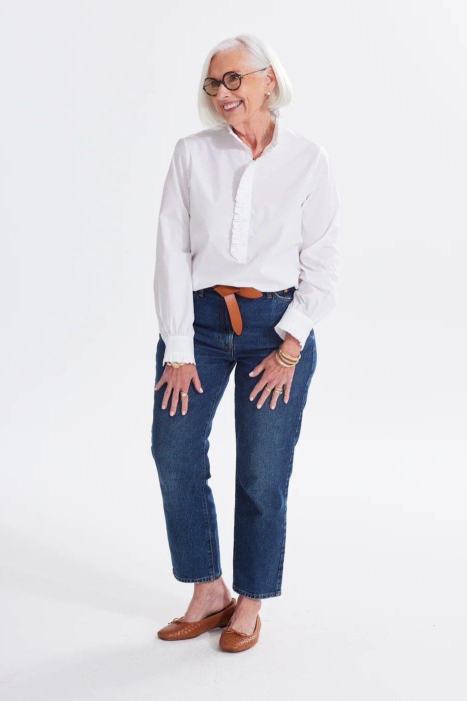 A white shirt with medium jeans and tan flats is clean and comfortable. Glasses add character to the simple look. White-haired women glow in crisp white. An easy everyday outfit.