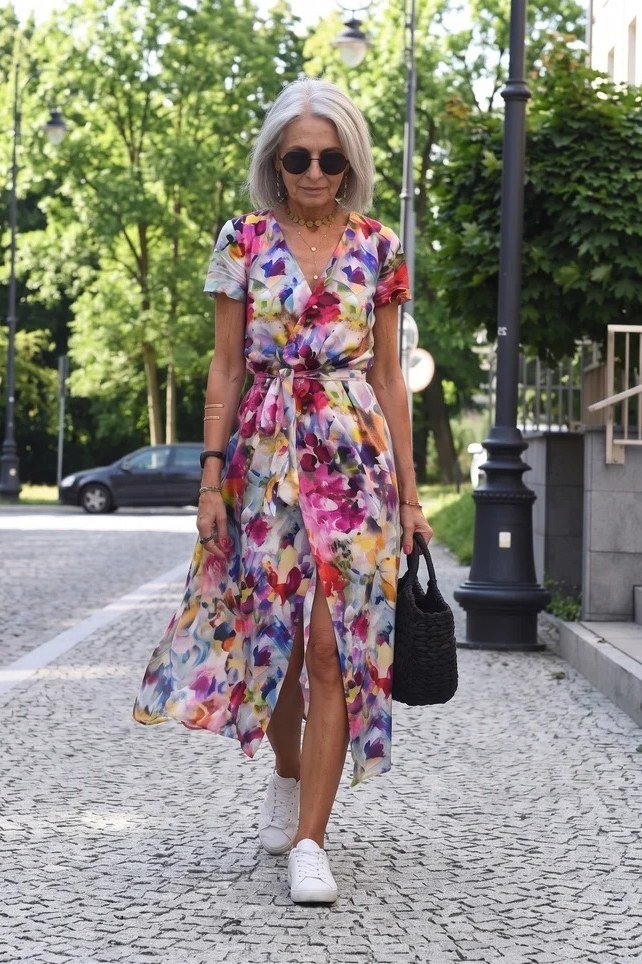 Colorful floral maxi dress with sunglasses and white sneakers on a city street, fun summer style for women over 60