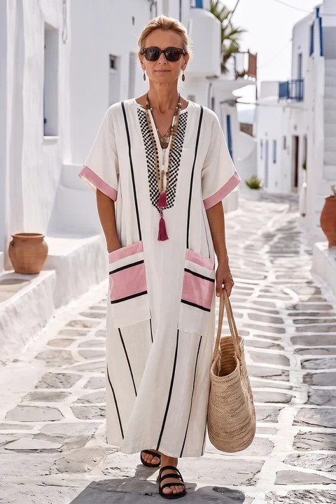 White embroidered caftan maxi dress with pink trim in a Greek alley, resort summer elegance for older women